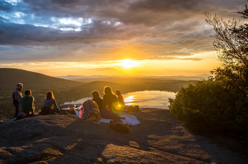 A group of people eating and drinking on top of a hill watching the sunset